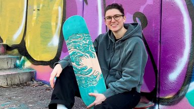 Junge Frau hält Skateboard, sitzend vor Graffitti Wand