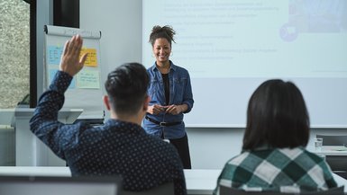 Eine Dozentin steht vor einer Klasse. Ein Teilnehmer meldet sich.