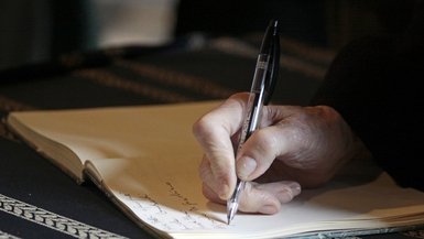 Hand von alter Person schreibt in ein Buch