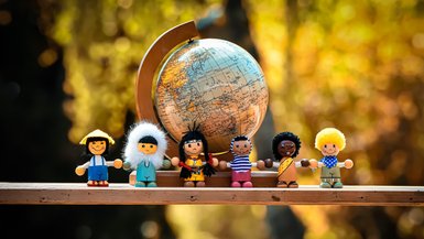 Sechs Spielzeugfiguren stehen vor einem kleinen Globus.